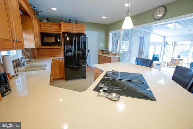 kitchen featuring a breakfast bar, light countertops, black appliances, pendant lighting, and a sink