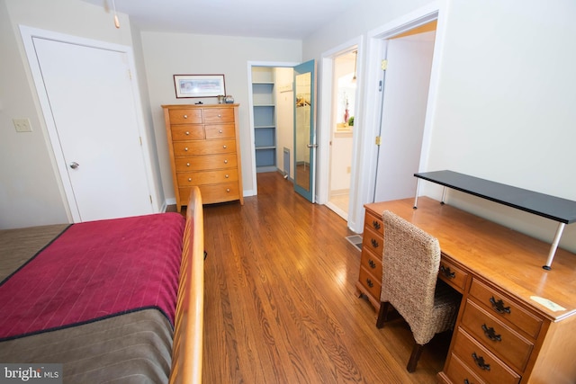 bedroom featuring a walk in closet, a closet, connected bathroom, and wood finished floors