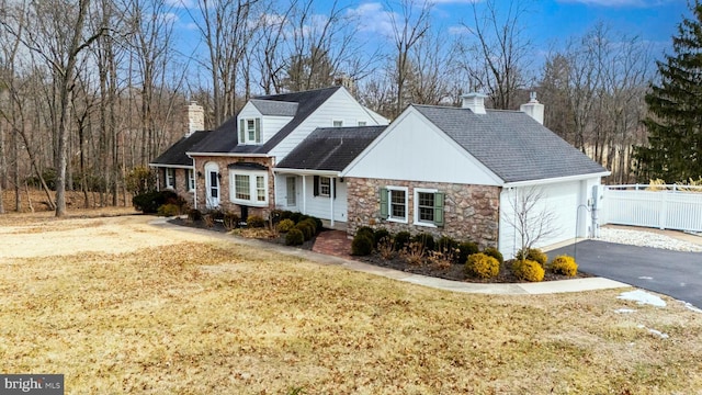 view of front facade featuring a chimney, an attached garage, stone siding, driveway, and a front lawn