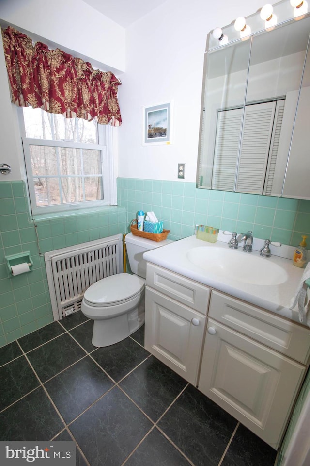 bathroom with tile walls, radiator, toilet, vanity, and tile patterned flooring