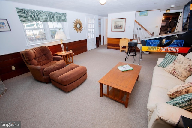 carpeted living room featuring wooden walls, stairway, and wainscoting