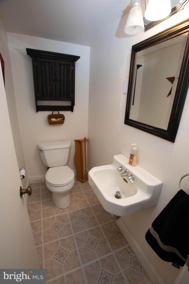 half bathroom with tile patterned flooring, a sink, toilet, and baseboards