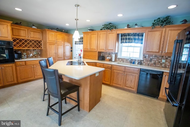 kitchen featuring decorative light fixtures, light countertops, a kitchen island, a sink, and black appliances