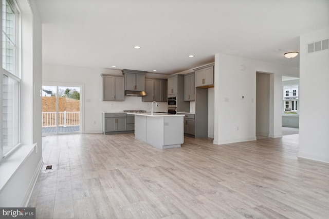 kitchen featuring gray cabinets, sink, light hardwood / wood-style floors, gas stovetop, and a center island with sink