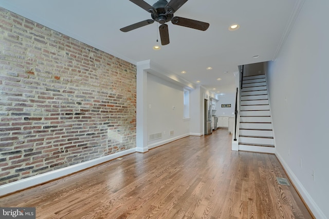 unfurnished living room with ornamental molding, brick wall, ceiling fan, and light hardwood / wood-style flooring