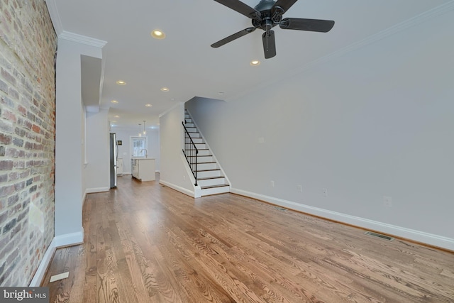 unfurnished living room with crown molding, brick wall, ceiling fan, and light hardwood / wood-style flooring