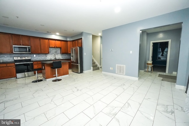 kitchen featuring a kitchen island, appliances with stainless steel finishes, sink, a kitchen bar, and decorative backsplash