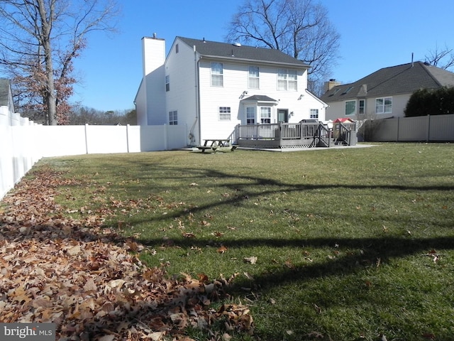 back of property with a deck, a fenced backyard, a lawn, and a chimney