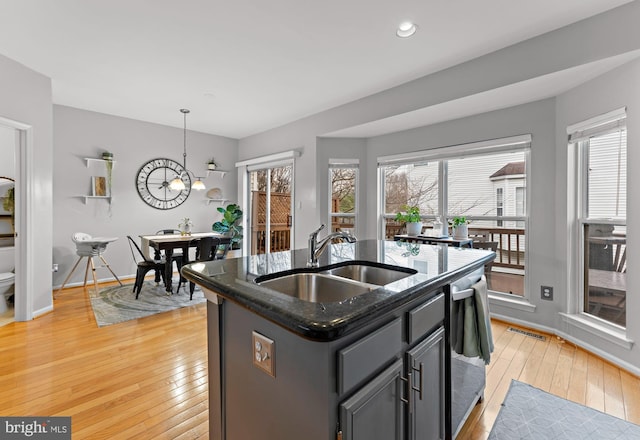 kitchen featuring dark stone countertops, visible vents, light wood finished floors, a sink, and stainless steel dishwasher