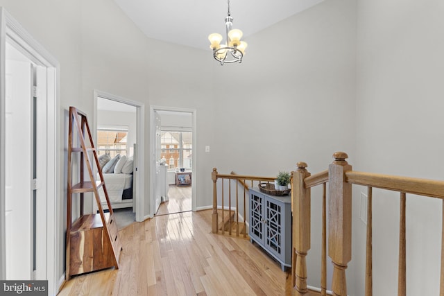 hallway featuring light wood-type flooring, an upstairs landing, baseboards, and a chandelier