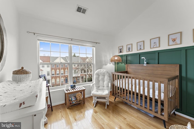 bedroom featuring visible vents, a crib, light wood-type flooring, and lofted ceiling