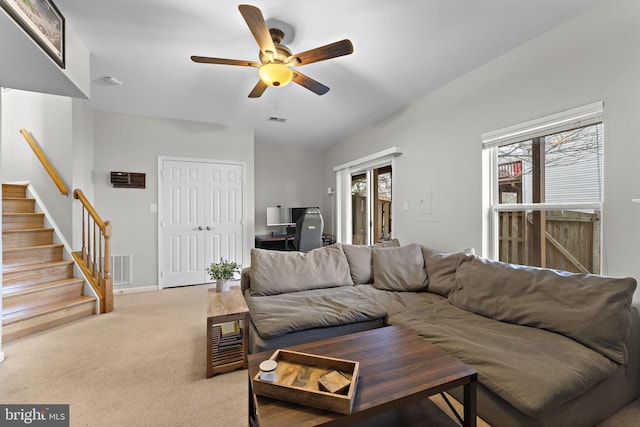 living area featuring light carpet, visible vents, stairs, and a ceiling fan