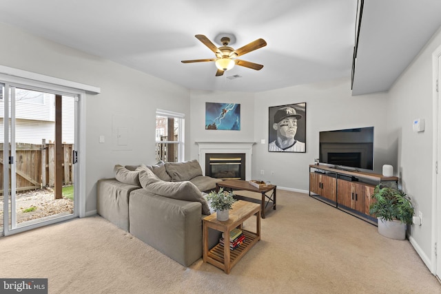 living area with a glass covered fireplace, carpet flooring, baseboards, and ceiling fan