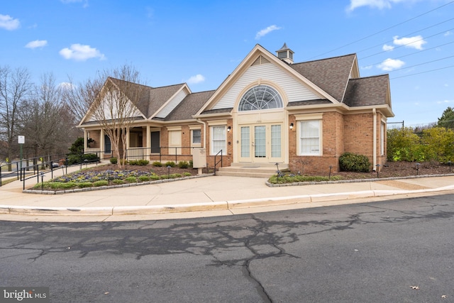 view of front of property with fence, french doors, brick siding, and roof with shingles