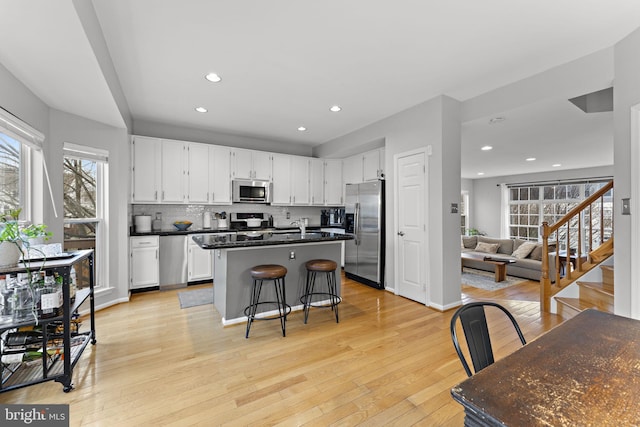 kitchen featuring an island with sink, decorative backsplash, white cabinets, light wood-style floors, and appliances with stainless steel finishes