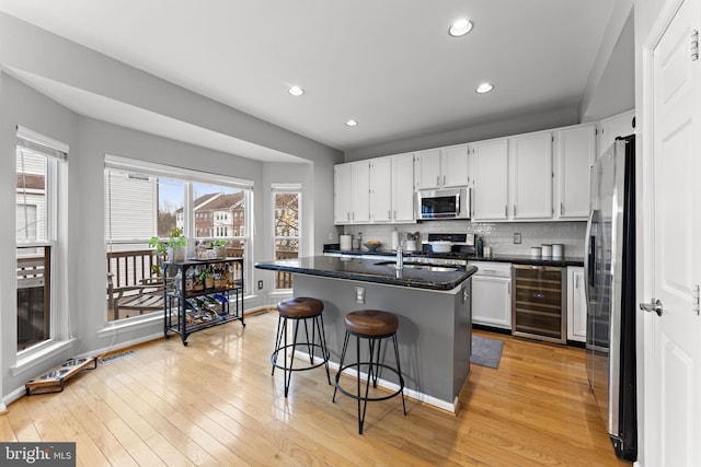 kitchen featuring decorative backsplash, wine cooler, white cabinets, appliances with stainless steel finishes, and light wood-type flooring