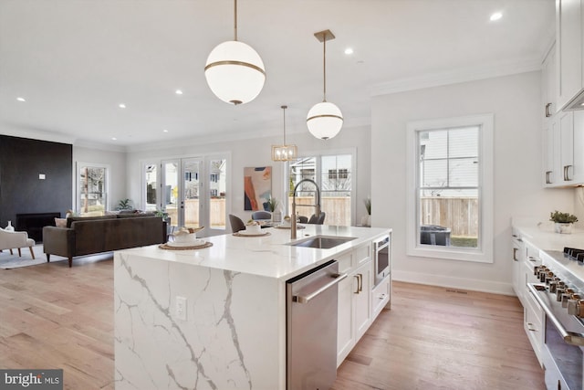 kitchen with sink, white cabinetry, decorative light fixtures, appliances with stainless steel finishes, and an island with sink