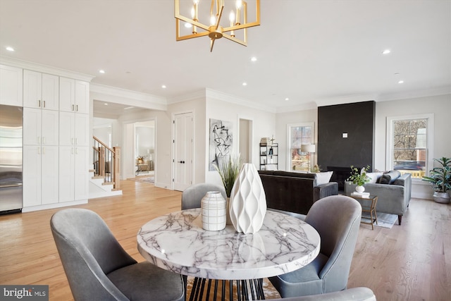 dining area with an inviting chandelier, crown molding, light hardwood / wood-style floors, and a large fireplace