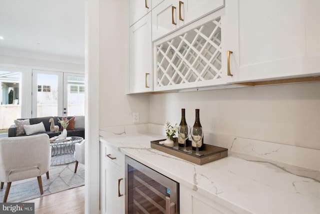 bar with light hardwood / wood-style flooring, ornamental molding, light stone countertops, and beverage cooler