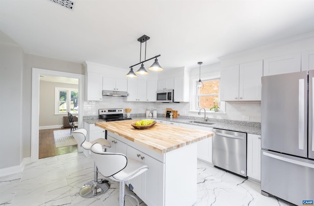 kitchen featuring stainless steel appliances, hanging light fixtures, a kitchen island, sink, and white cabinets