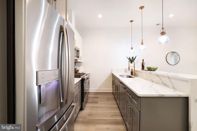 kitchen with decorative light fixtures, gray cabinetry, stainless steel appliances, light stone countertops, and light wood-type flooring