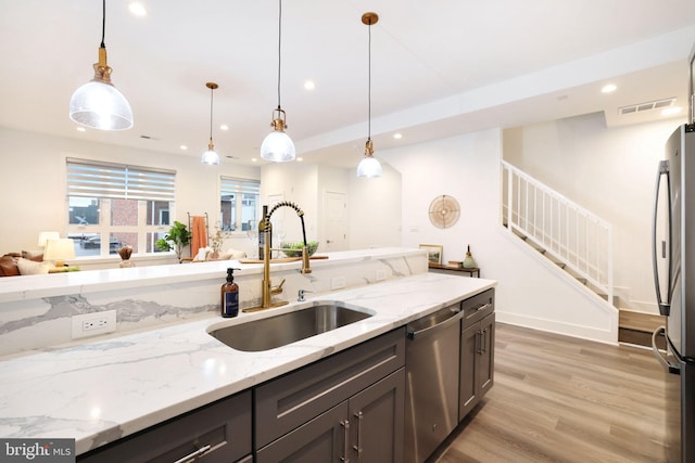 kitchen featuring pendant lighting, stainless steel appliances, sink, and light stone counters