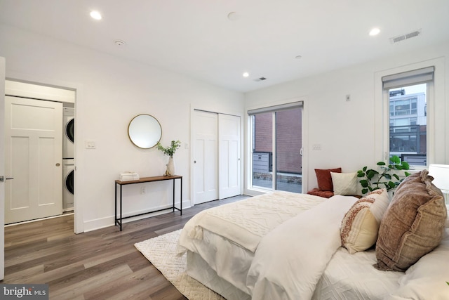 bedroom with hardwood / wood-style flooring, stacked washer and clothes dryer, and access to outside