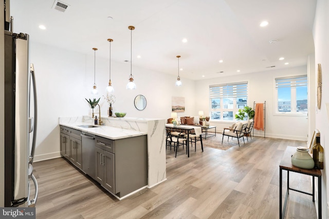 kitchen featuring sink, light stone counters, decorative light fixtures, gray cabinets, and stainless steel appliances