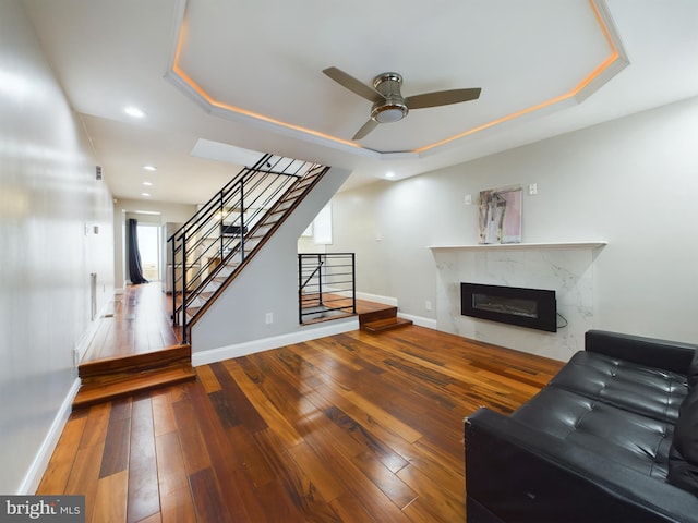 living room with a raised ceiling, ceiling fan, hardwood / wood-style flooring, and a high end fireplace