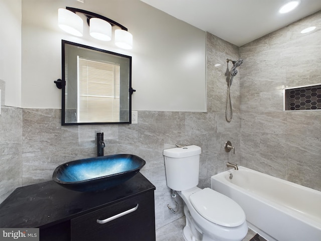 full bathroom with tiled shower / bath, vanity, toilet, and tile walls