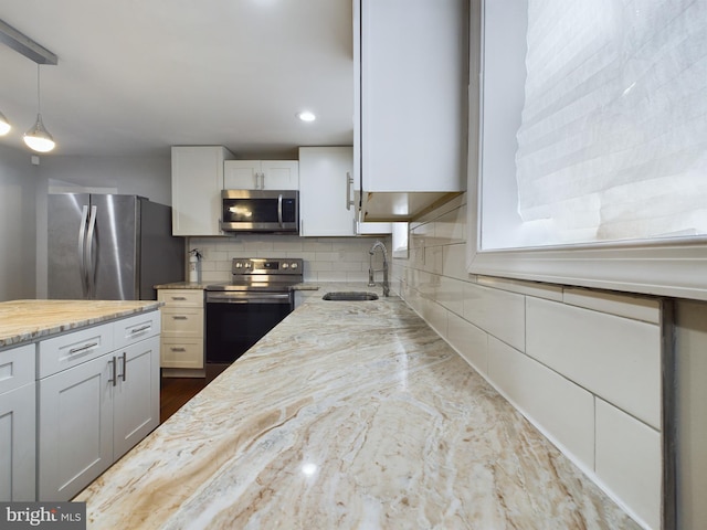 kitchen with appliances with stainless steel finishes, decorative light fixtures, sink, white cabinets, and backsplash