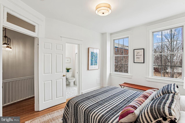 bedroom with multiple windows, connected bathroom, and hardwood / wood-style flooring