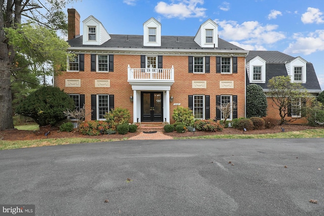 colonial-style house featuring french doors, brick siding, a chimney, and a balcony