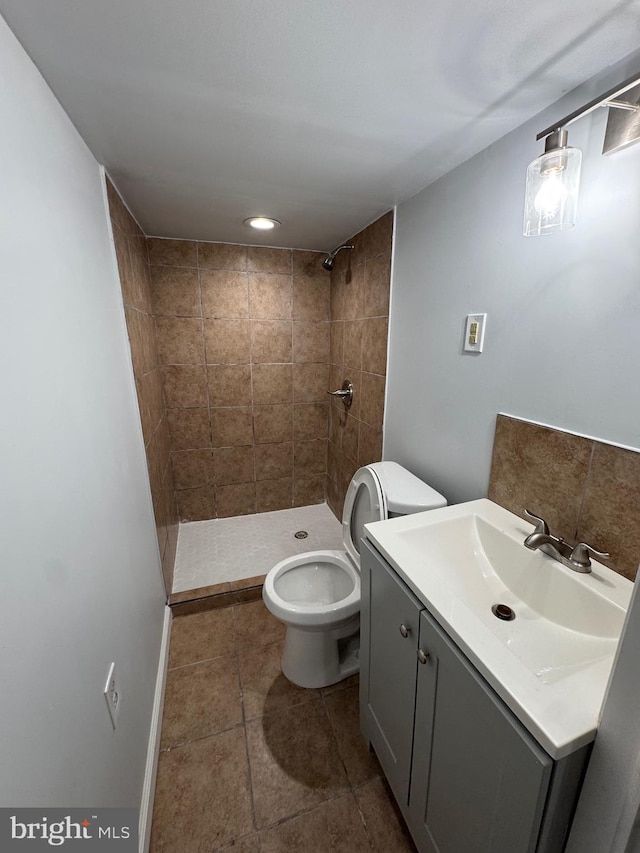 bathroom with a tile shower, vanity, and toilet