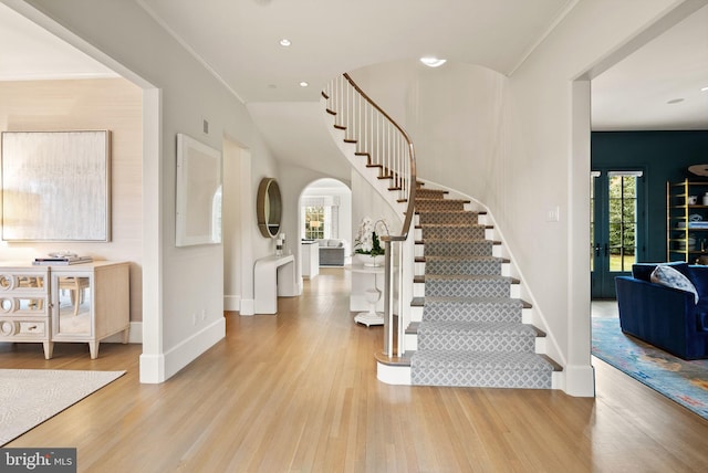 foyer featuring a healthy amount of sunlight, stairway, arched walkways, and wood finished floors