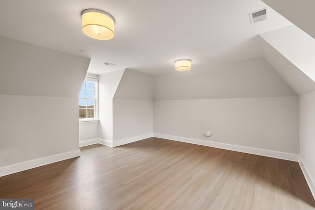 additional living space featuring lofted ceiling, wood finished floors, visible vents, and baseboards