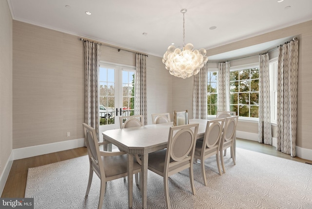 dining space with wallpapered walls, baseboards, light wood-style flooring, crown molding, and a chandelier