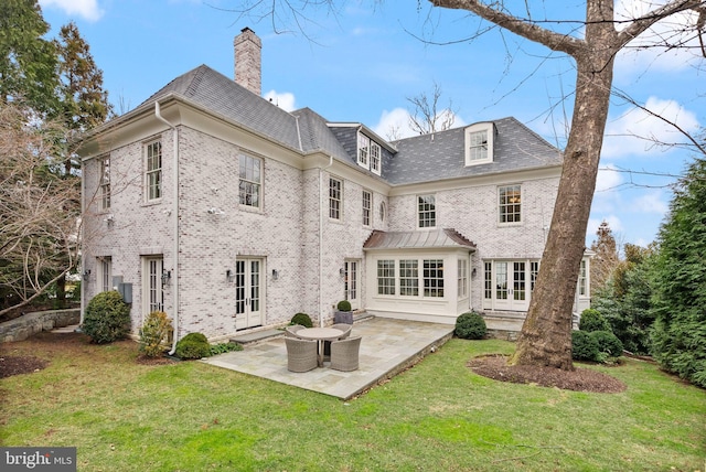 back of house featuring french doors, brick siding, a lawn, and a chimney