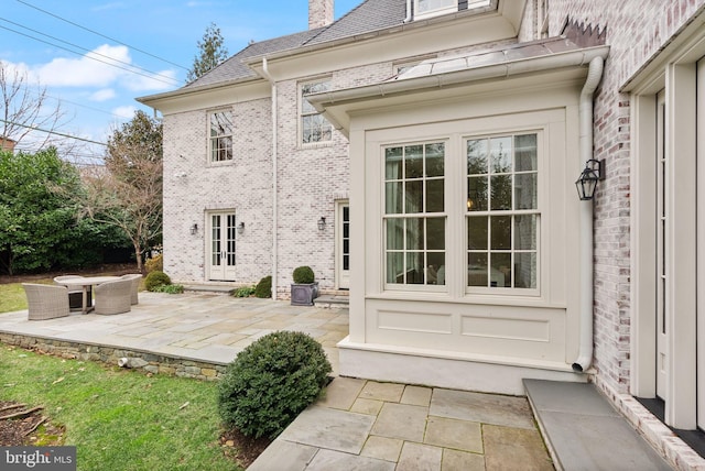 entrance to property featuring a patio, brick siding, and a chimney