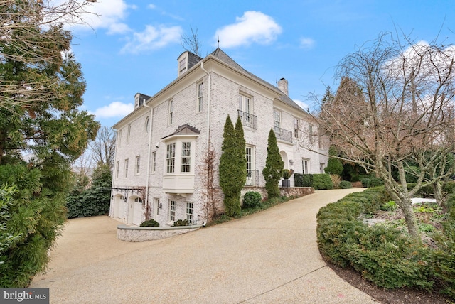 view of side of property with driveway, an attached garage, a chimney, and brick siding