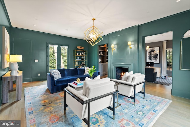 living area with a warm lit fireplace, a notable chandelier, wood finished floors, and french doors