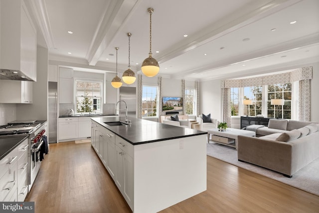 kitchen featuring premium appliances, dark countertops, a sink, beamed ceiling, and wall chimney exhaust hood