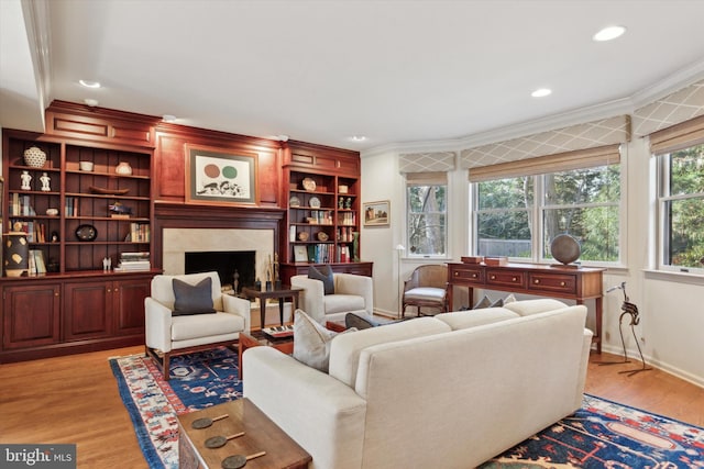 living area featuring crown molding, baseboards, recessed lighting, a high end fireplace, and light wood-style flooring