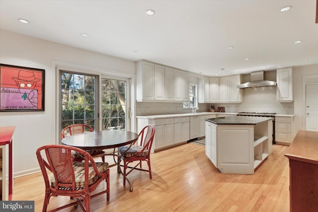 kitchen with light wood-type flooring, backsplash, wall chimney range hood, and a center island