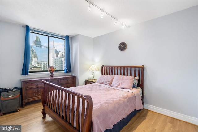 bedroom featuring baseboards, track lighting, a view of city, and light wood-style floors