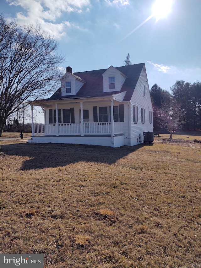 view of front of home with a porch, a chimney, a front lawn, and central air condition unit