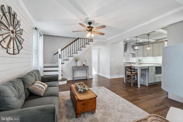 living area featuring a ceiling fan, baseboards, stairs, ornamental molding, and dark wood-style floors