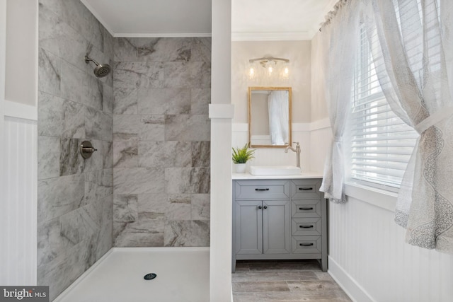 bathroom with a wainscoted wall, ornamental molding, wood finished floors, a tile shower, and vanity