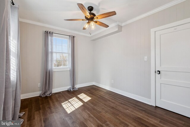 empty room with dark wood-style flooring, visible vents, ornamental molding, ceiling fan, and baseboards