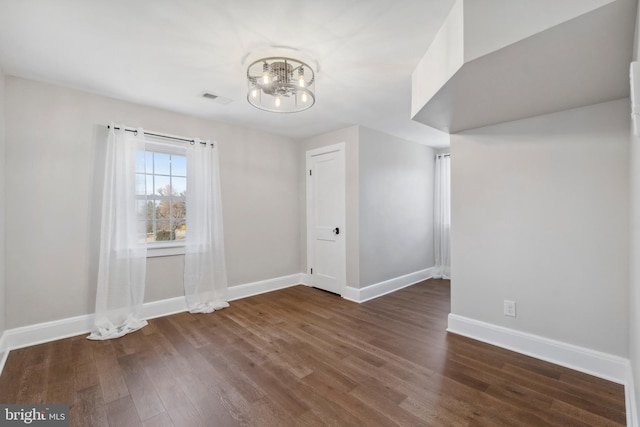 empty room featuring baseboards, visible vents, a chandelier, and wood finished floors